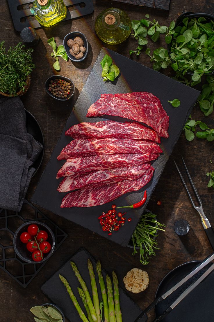 raw meat on a cutting board surrounded by vegetables and seasonings, including asparagus