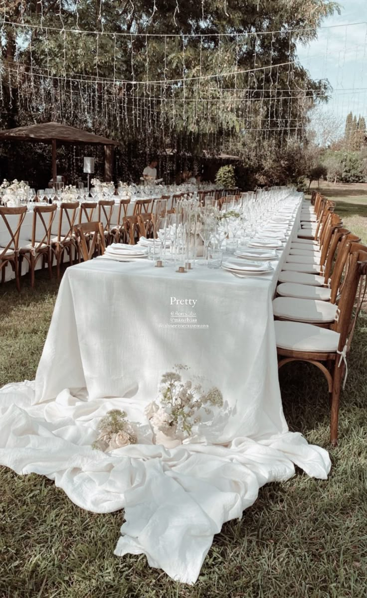 a long table is set up with white linens and place settings for an outdoor dinner