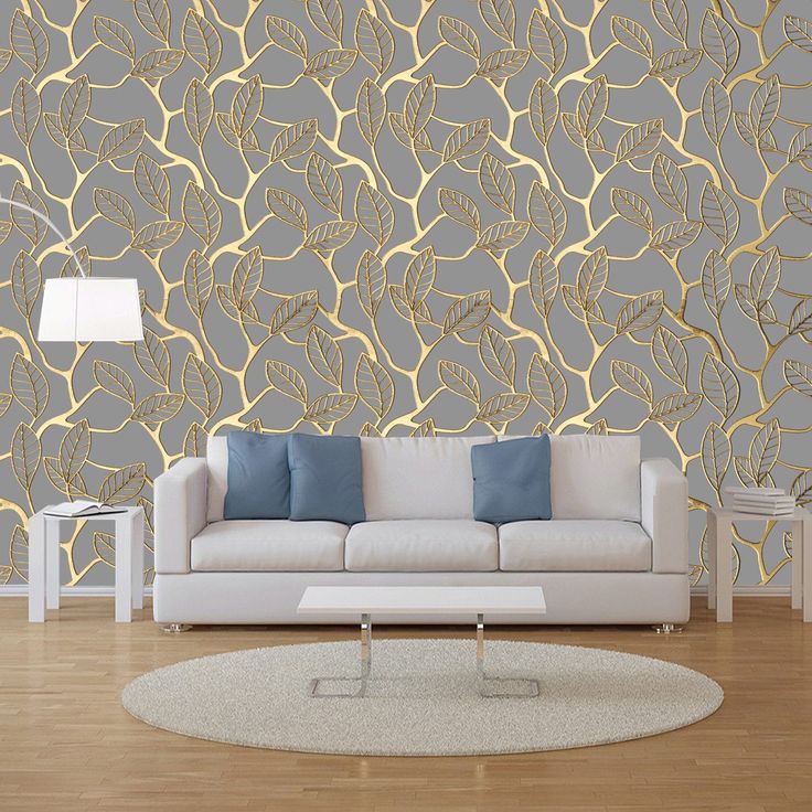 a white couch sitting in front of a wall with gold leaves on it and blue pillows