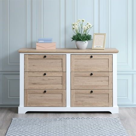 a white and wood dresser with flowers on top in front of a blue painted wall