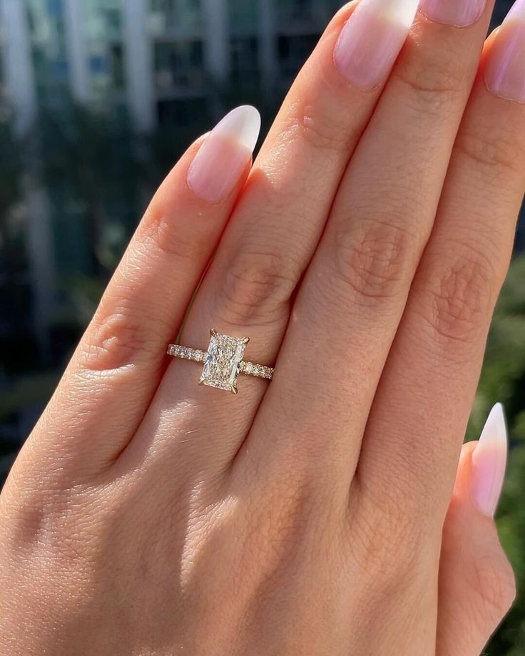 a woman's hand with a diamond ring on top of her finger and the other hand holding an engagement ring