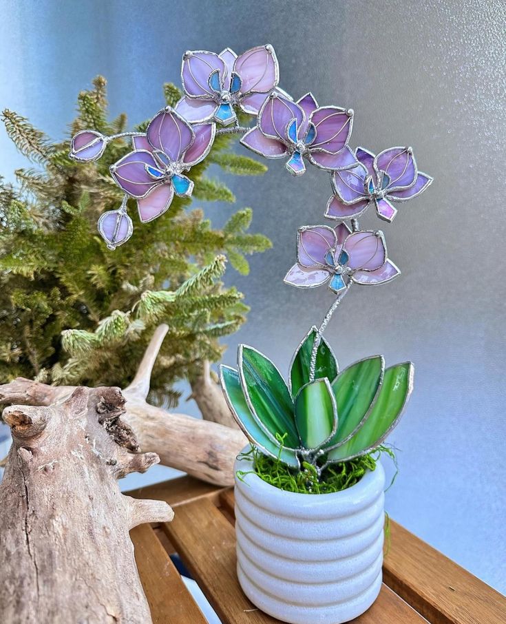 purple flowers are in a white vase on a wooden table next to a driftwood branch