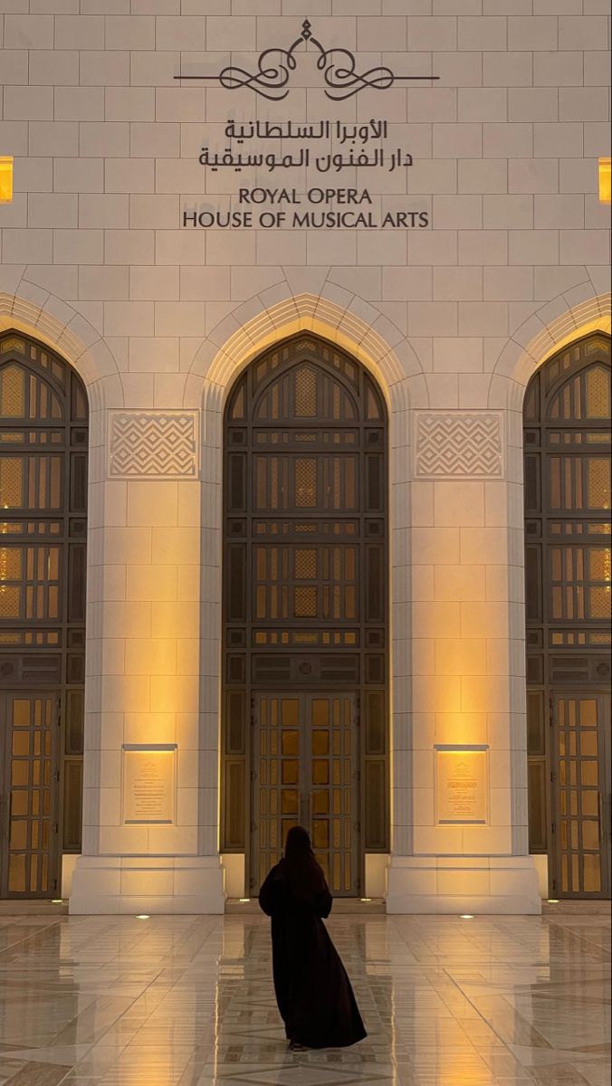 a woman standing in front of a building with two doors and lights on the walls