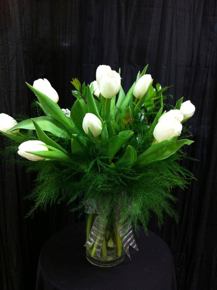 a vase filled with white tulips on top of a black cloth covered table