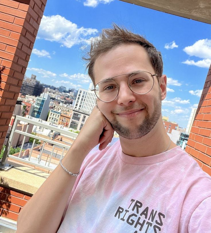 a man wearing glasses standing in front of a brick building