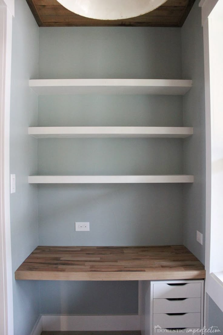 an empty room with white shelves and wooden desk