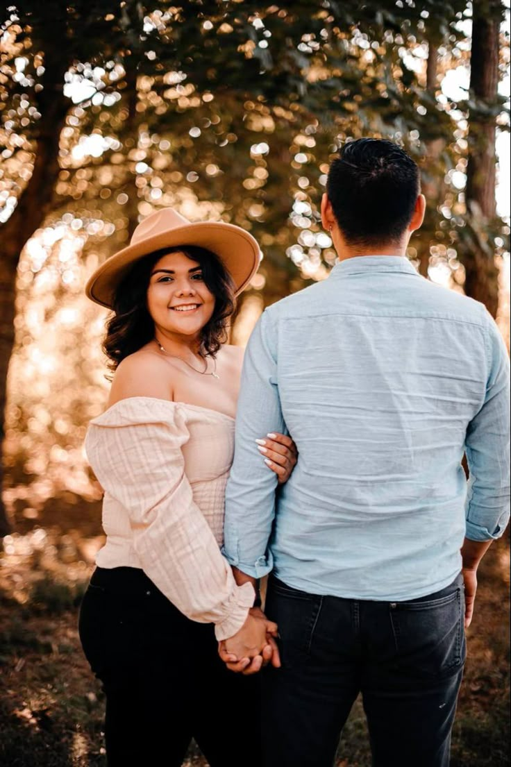 a man and woman standing next to each other holding hands in front of some trees