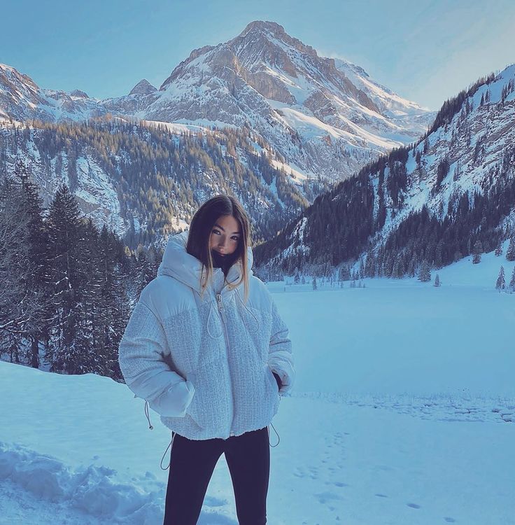 a woman standing on top of a snow covered slope in front of mountains and trees