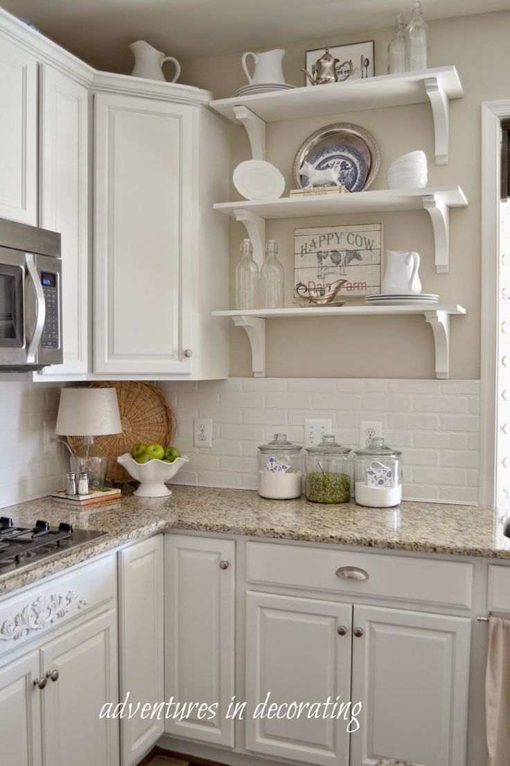 a kitchen with white cabinets and open shelving on the wall above the stove top