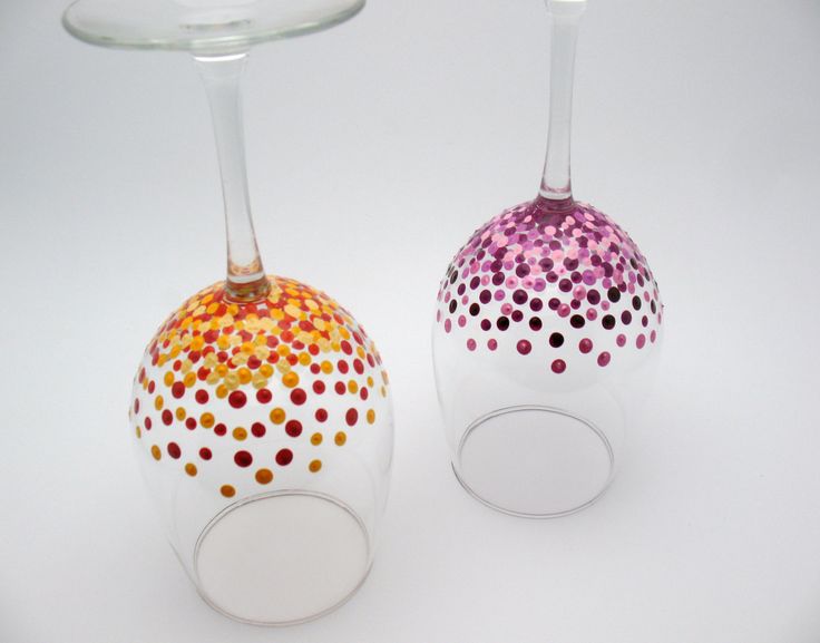 two wine glasses with colorful dots on them sitting next to each other in front of a white background