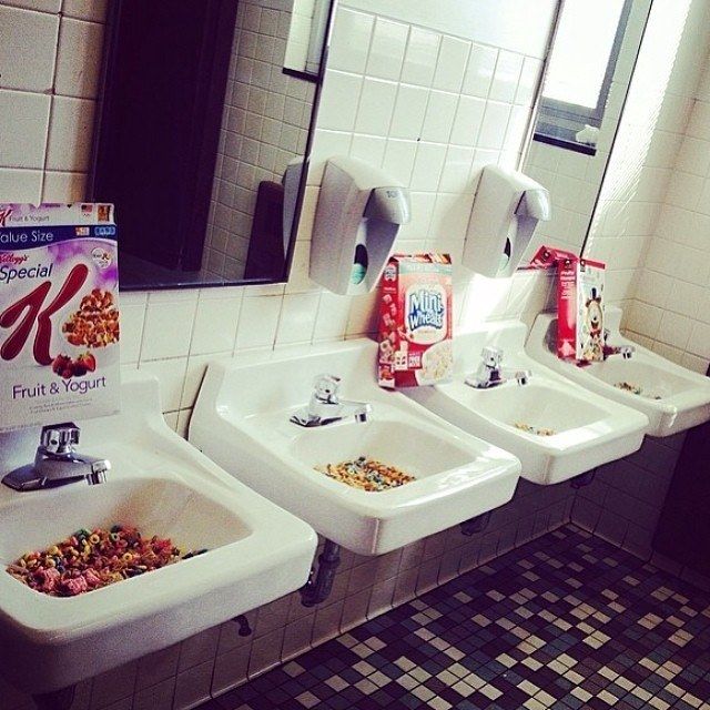 three sinks in a public restroom with cereal on the sink and candy bars on the counter