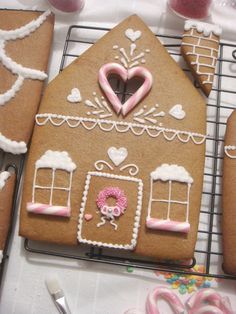 gingerbread house decorated with pink icing and white frosting on a cooling rack