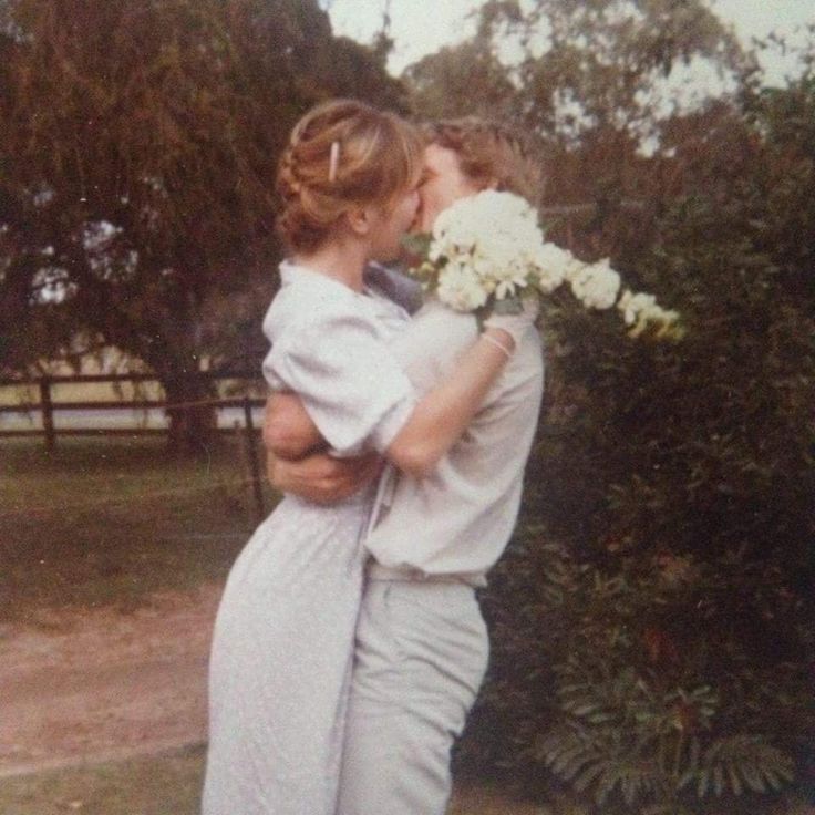 a man and woman embracing each other in front of some trees with white flowers on them