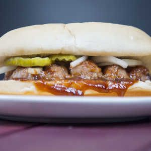 a meatball sub sandwich with pickles and ketchup on a white plate