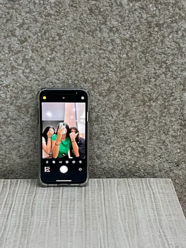 an iphone sitting on top of a table next to a gray wall with two people taking pictures