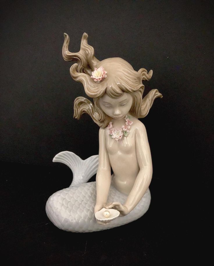 a ceramic figurine of a mermaid sitting on top of a white fish with her hair blowing in the wind