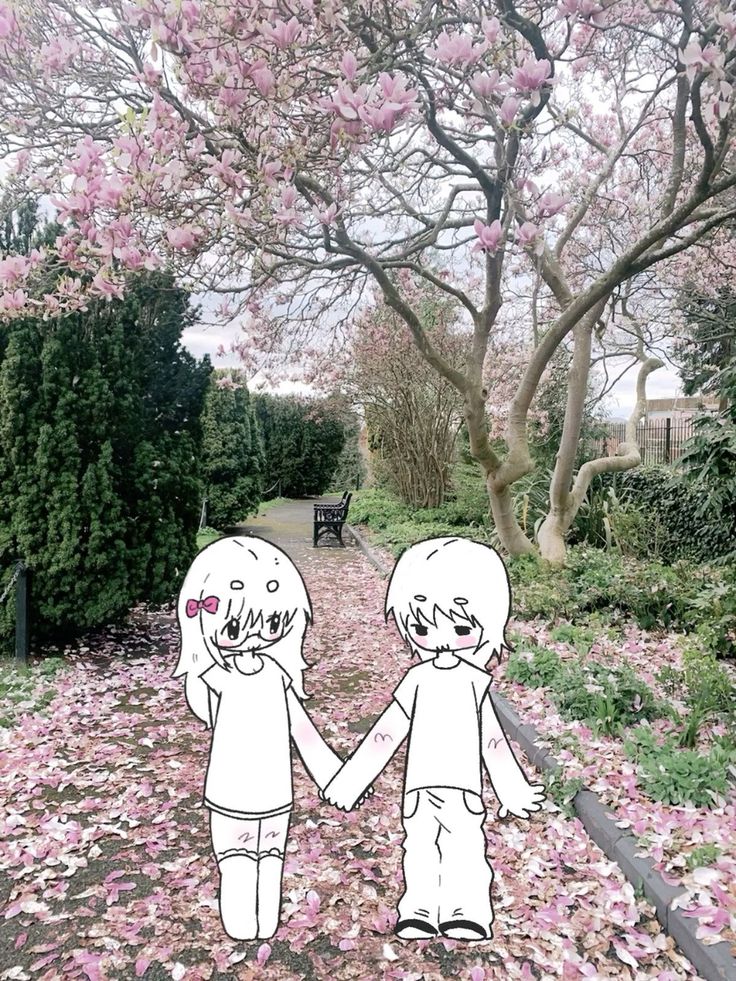 two people holding hands while walking down a path covered in pink flowers and trees with leaves on the ground