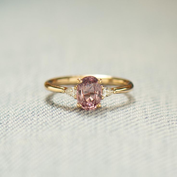 a pink diamond ring sitting on top of a white cloth covered table with a light colored background