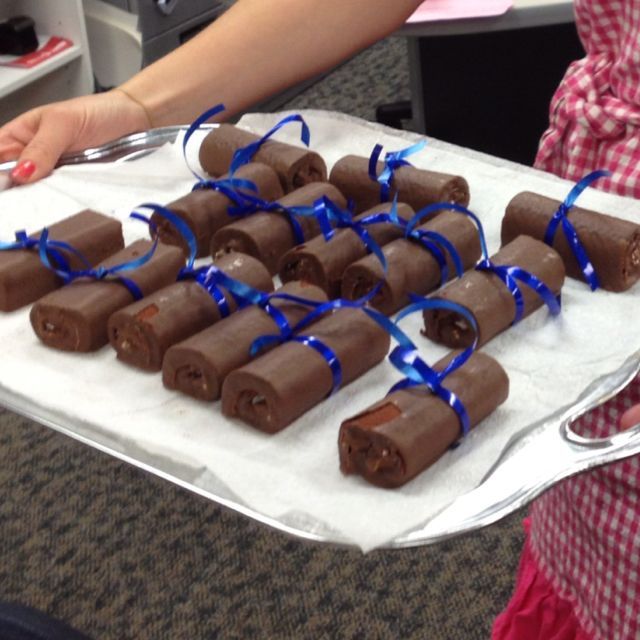 a woman holding a tray full of chocolates on top of a table with blue ribbons