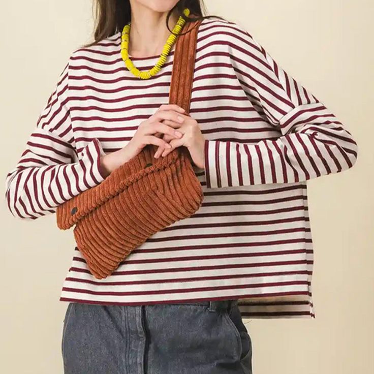 a woman wearing a striped shirt and holding a brown knitted handbag in front of her face