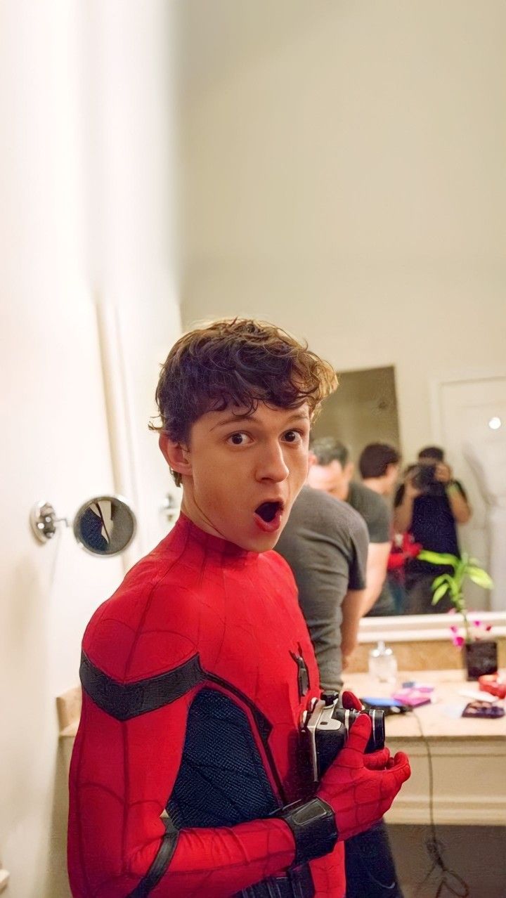 a young man dressed as spider - man holding a camera and making a surprised face