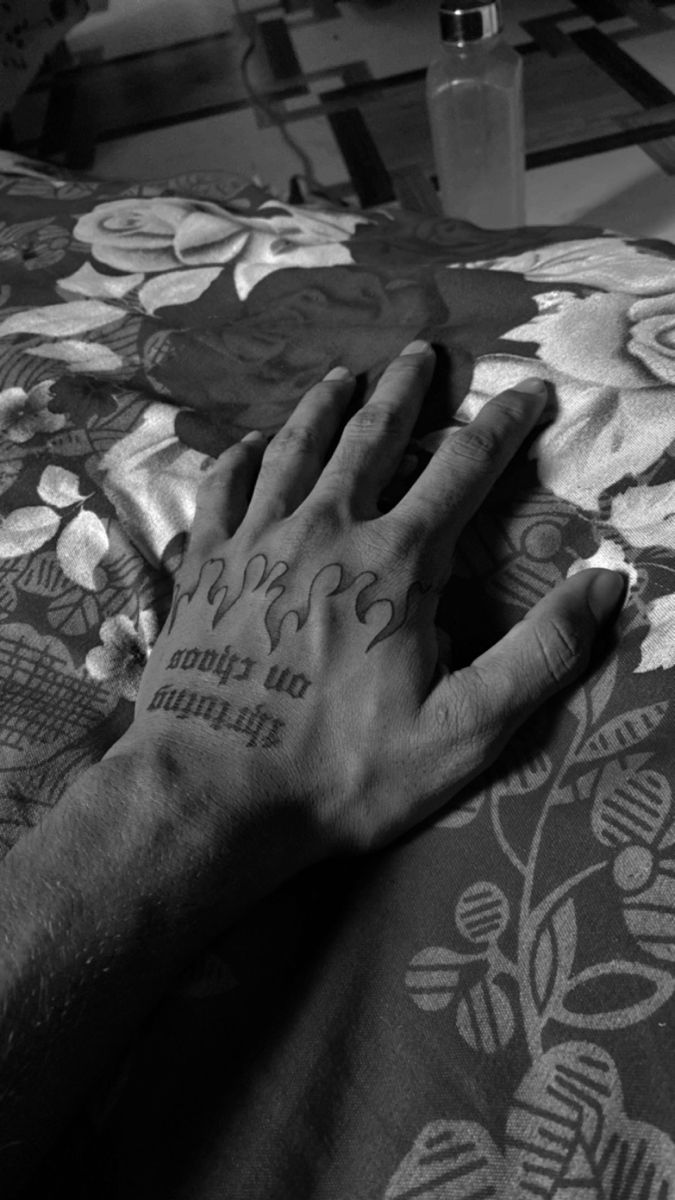 a person's hand with tattoos on it laying on a bed next to a bottle