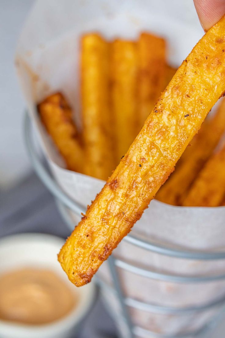 a person holding up a piece of french fries in front of some dipping sauces