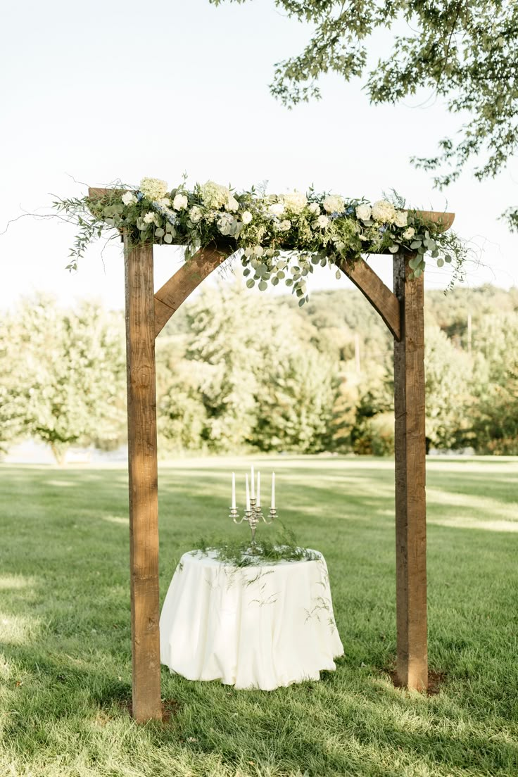 an outdoor wedding ceremony setup with white flowers and greenery on the top of a wooden arch