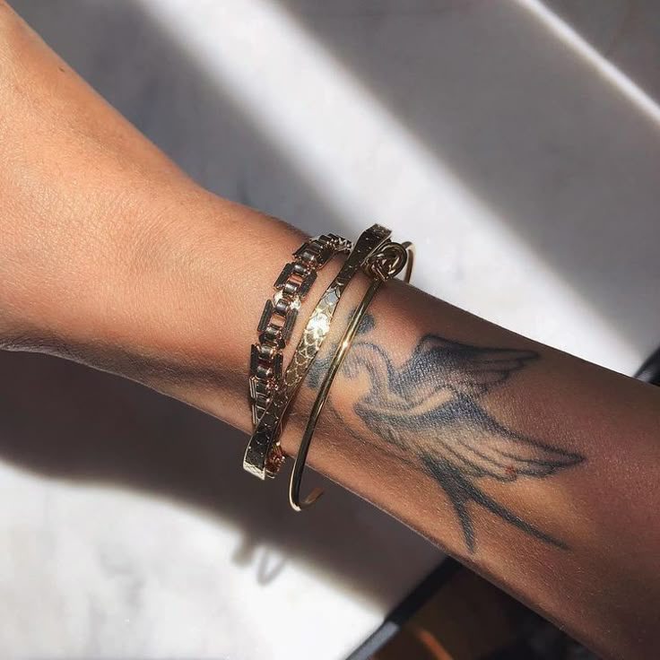 a woman's arm with tattoos and bracelets on her left wrist, holding onto a piece of jewelry