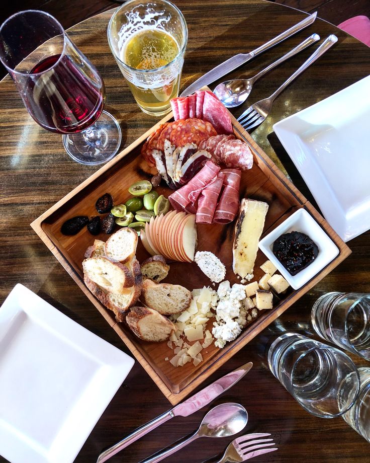 a wooden table topped with lots of different types of food and wine glasses on top of it