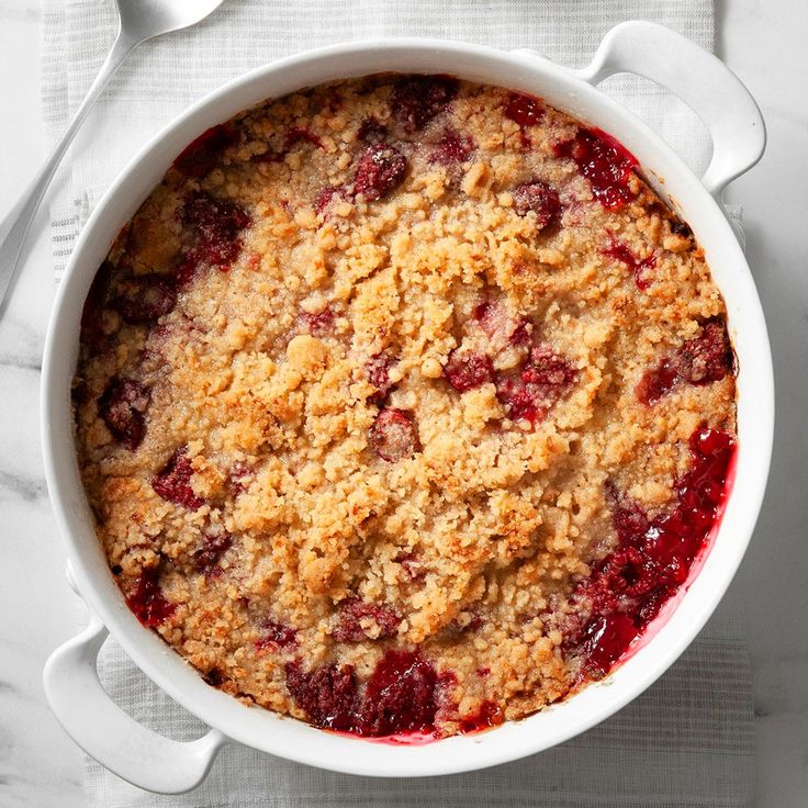 a white dish filled with crumbled fruit on top of a table next to utensils