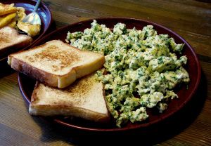 two plates filled with toast and vegetables on top of a wooden table next to a bowl of fries