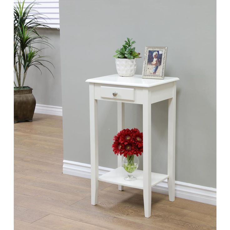 a small white table with flowers on top and a potted plant next to it