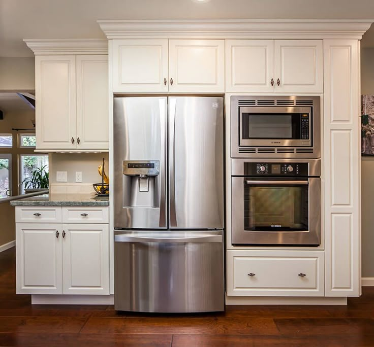 a stainless steel refrigerator and oven in a kitchen with white cabinets, wood floors and hardwood flooring