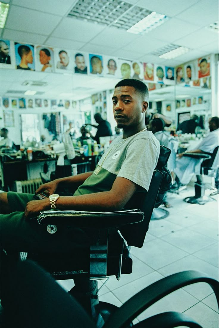 a man sitting in a barbershop with his haircuts and other people behind him