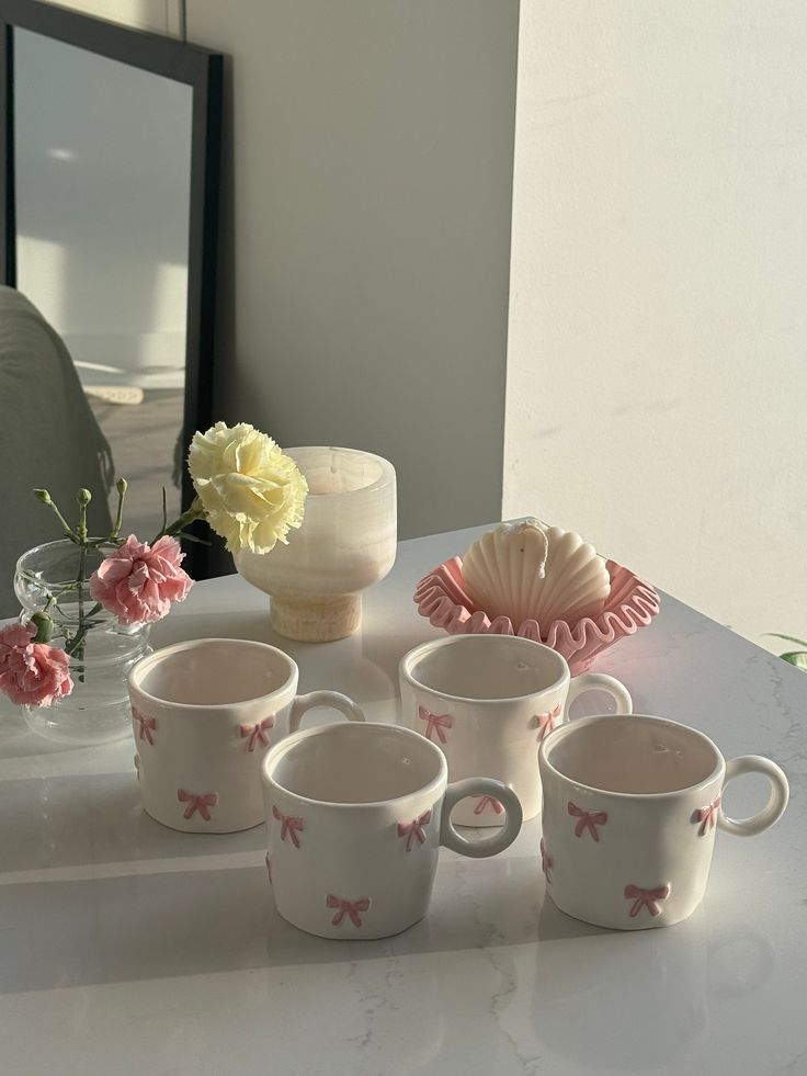 four coffee mugs sitting on a table with flowers in front of a large mirror