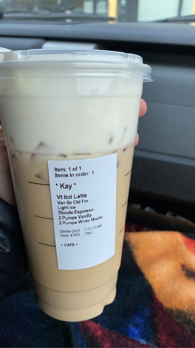 a person holding up a cup of iced coffee in their hand with the label on it