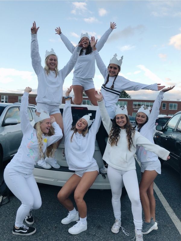 four girls in white outfits standing on the back of a car with their arms up