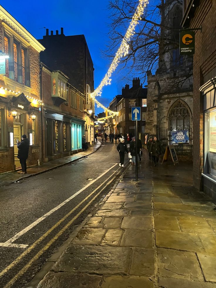 people walking down the street at night with christmas lights strung across the buildings on both sides