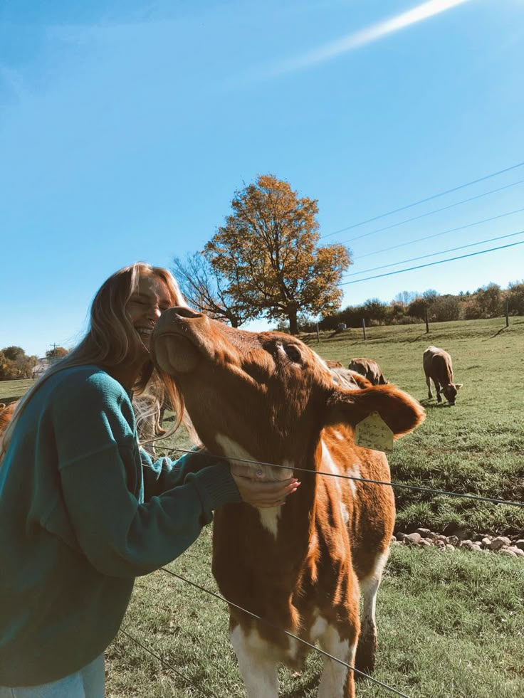 a woman standing next to a brown and white cow on top of a lush green field