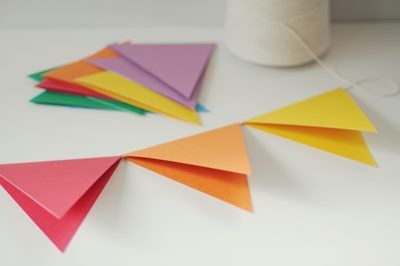 several colored paper triangles on a white surface next to a spool of thread and a ball of yarn