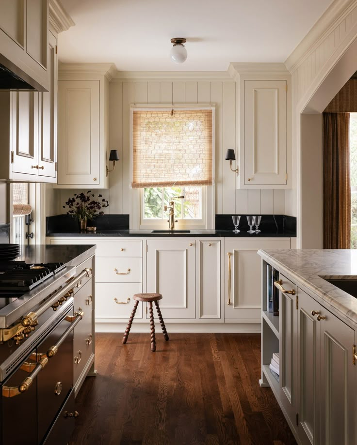 a kitchen with wooden floors and white cabinets, black counter tops and gold trimmings