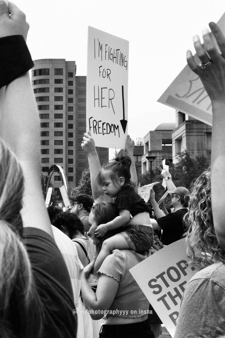 a group of people holding signs in the air with one child on their shoulders and another woman hugging her head