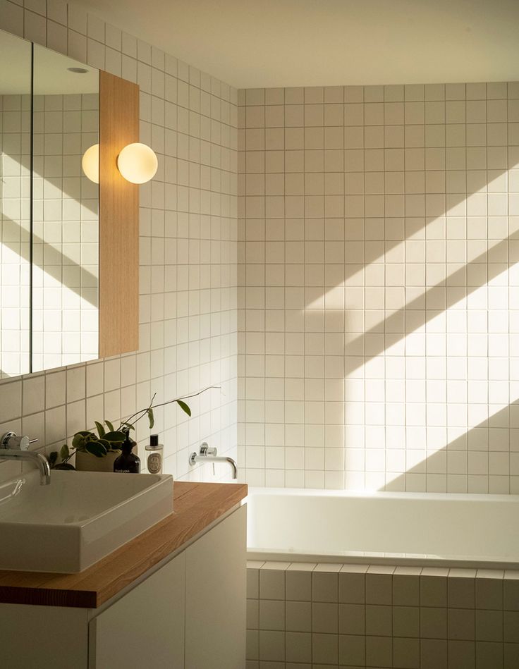 a bathroom with a sink, mirror and bathtub next to a wall mounted light fixture