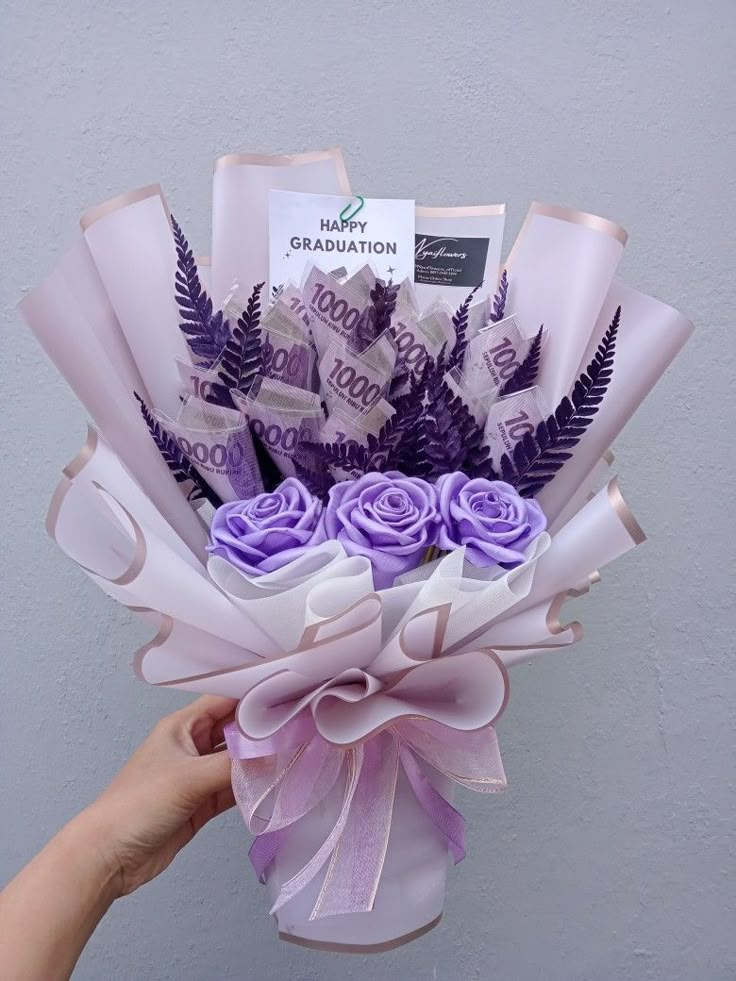 a hand holding a bouquet of flowers with congratulations written on the front and purple ribbon around it