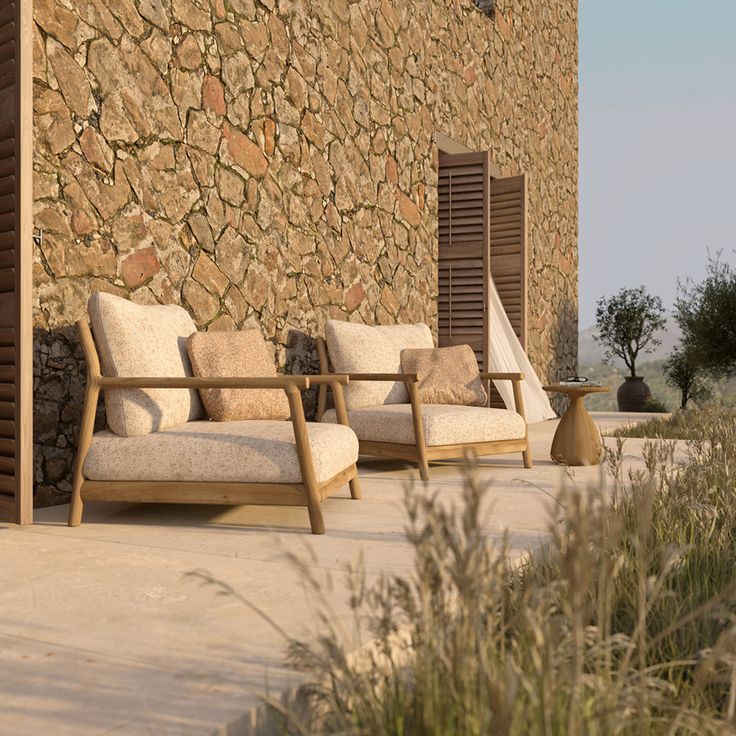 two wooden chairs sitting next to each other near a stone wall