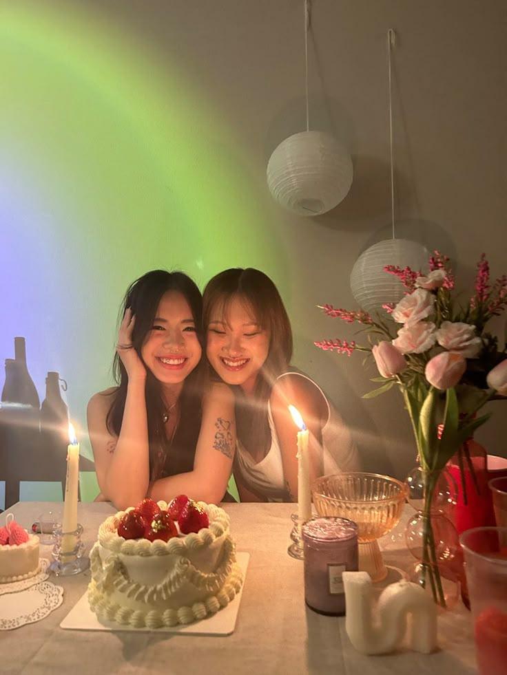 two young women sitting at a table with a cake and candles in front of them