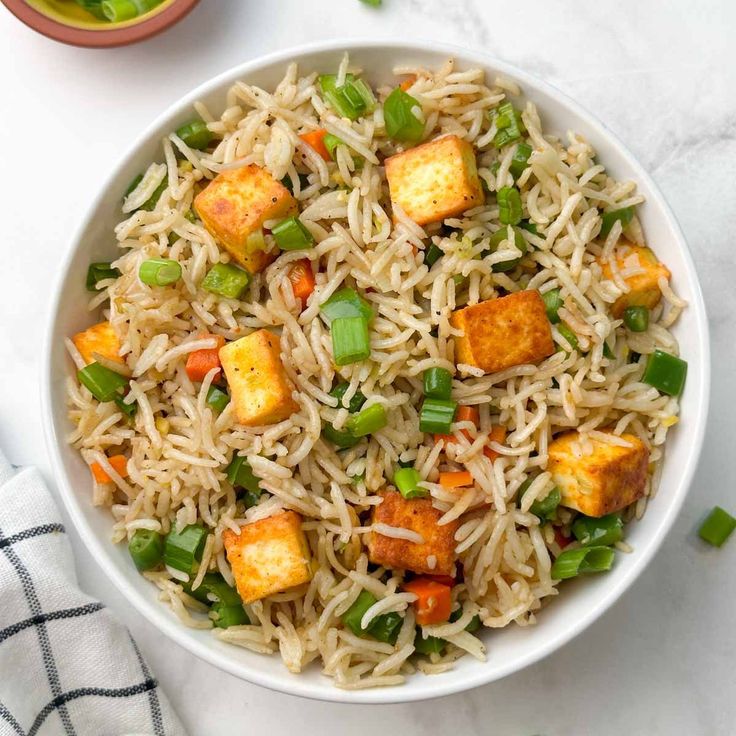 a white bowl filled with rice, tofu and green onions on top of a table