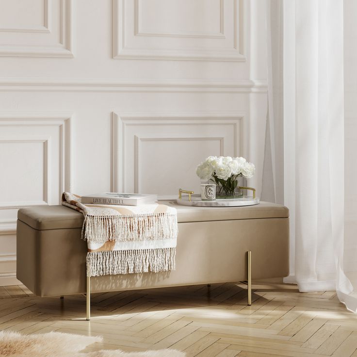 a white flower vase sitting on top of a bench next to a window with curtains