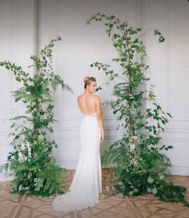 a woman in a white dress standing next to some green plants and greenery on the wall